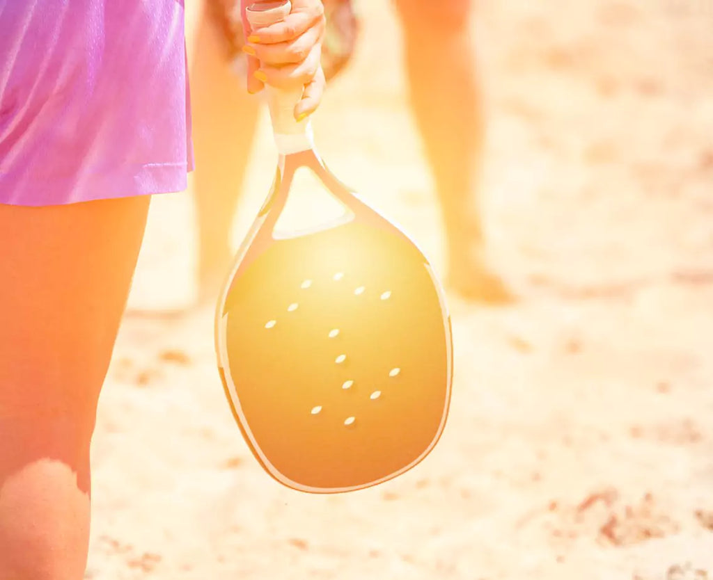 iamBeachTennis resource learning center - image of a female beach tennis player holding a beach tennis paddle face down while standing on a sand beach tennis court