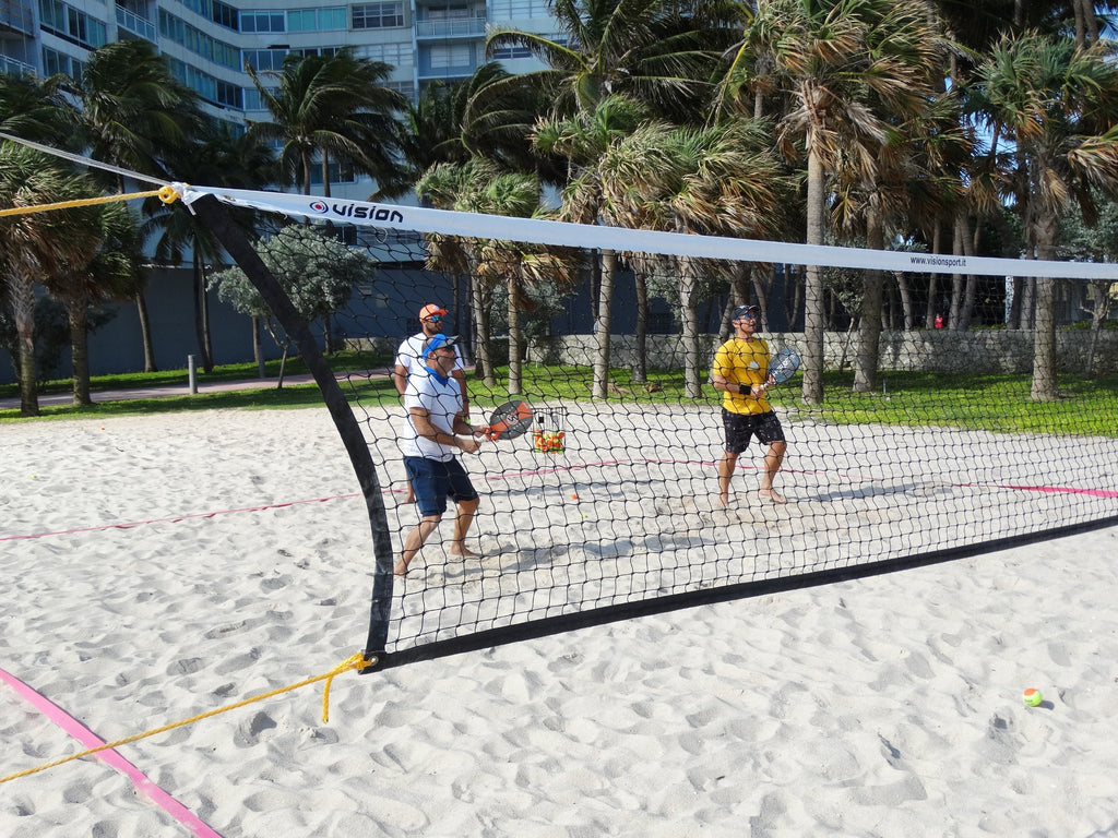 iamBeachTennis online store - image of three beach tennis players training, image is looking though a beach tennis net at the players in active play on a beach tennis sand court