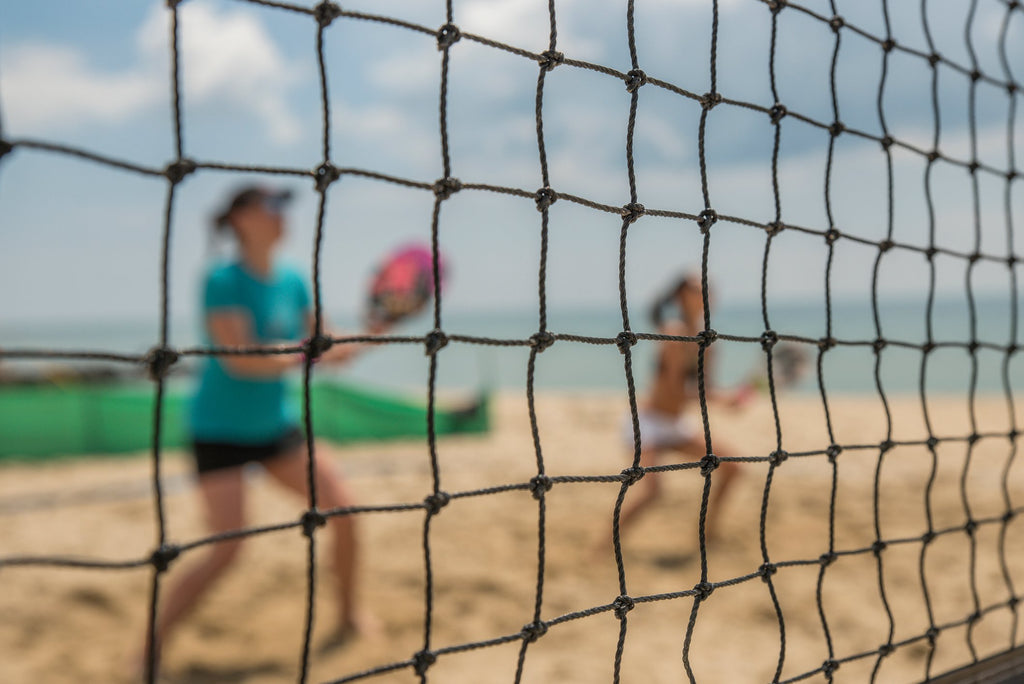 to female beach tennis players on a beach tennis court. View is though the beach tennis net.