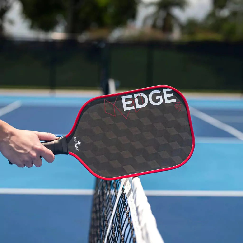SPORT: PICKLEBALL. Shop Diadem Sports Pickleball at "iamPickleball.Store" a division of "iamracketsports.com". Racket model is a 2023 Diadem Edge 18K advanced/professional Pickleball Paddle. Paddle is in vertical position. Paddle on a pickleball net.