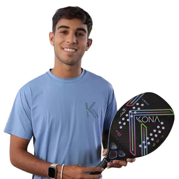 Player holding a Leo Branco signature   Kona K-DOZE BLUE GLOSSY 2024 Beach Tennis Paddle with Carbon 12K, glossy surface, Eva Soft core, 22mm thick. Shop Kona at i am Beach Tennis store.