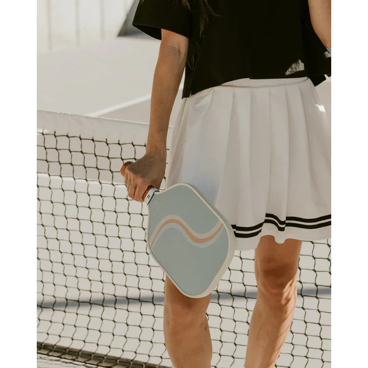 SPORT:PICKLEBALL.Shop Holbrook Pickleball at "iamracketsports.com" in Miami.  Racket model is a 2023 Holbrook PERFORMANCE REWIND pickleball paddle/racket for intermediate players.  Racquet/Paleta is in being held by standing female player on court.
