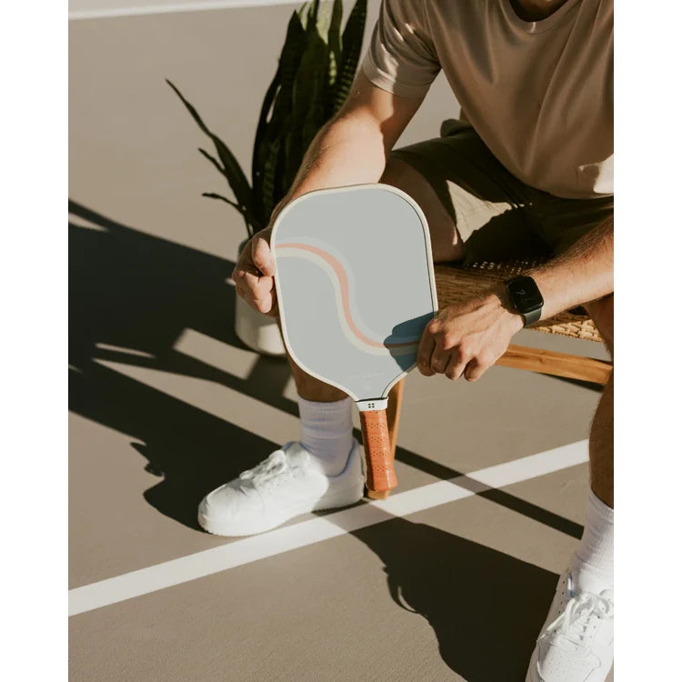SPORT:PICKLEBALL.Shop Holbrook Pickleball at "iamracketsports.com" in Miami.  Racket model is a 2023 Holbrook PERFORMANCE REWIND pickleball paddle/racket for intermediate players.  Racquet/Paleta is held by sitting male player on court.