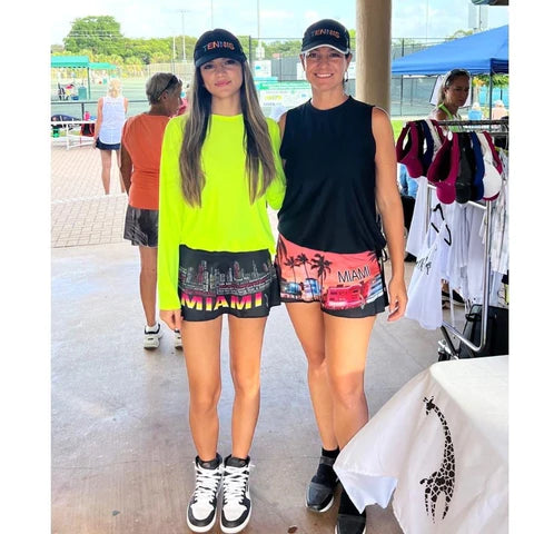 SPORT: PICKLEBALL. Shop Lacoa Sports clothing at "iamracketsports.com" in Miami.  Two female pickleball players at courts wearing black MIAMI SKYLINE Skirt printed with Miami Skylines described in text  and the city name shown, using vibrant neon yellow, pink and white.
