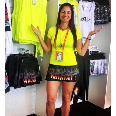 SPORT: PICKLEBALL. Shop Lacoa Sports clothing at "iamracketsports.com", Miami, FL, USA.  Front view of Lacoa's black MIAMI SKYLINE Skirt, with design of Miami Skylines described in text and the city name  shown, using vibrant neon yellow, pink and white.